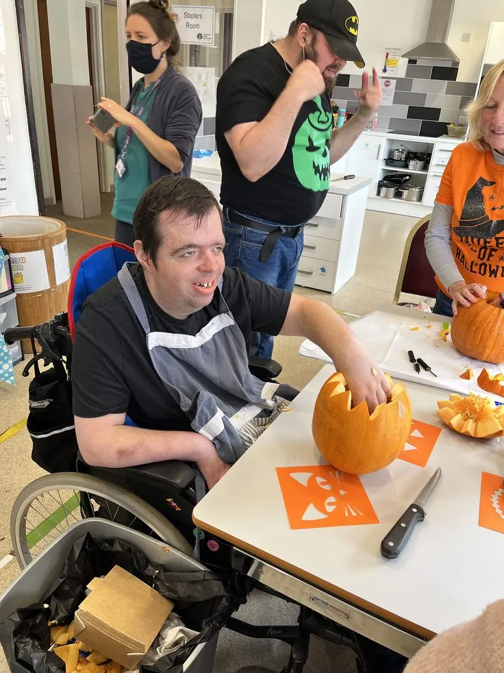A participant preparing food at a kitchen table alongside his support workers